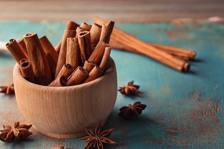 Wooden bowl with cinnamon sticks and anise on table