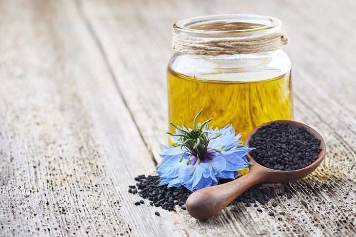 Black cumin oil with flower nigella sativa on wooden board