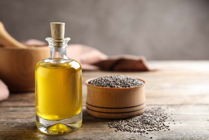 Bottle of chia oil and bowl with seeds on table. Space for text