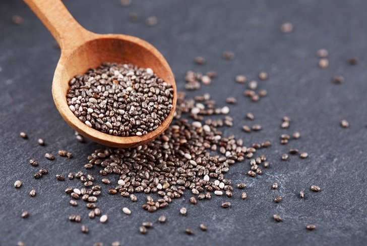 Chia seeds in wooden spoon, lying on dark stone background.