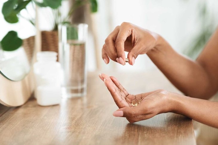 Unrecognizable African Woman Taking Beauty Supplements For Glowing Skin, Holding Omega-3 Fish Oil Capsules In Hands, Side View