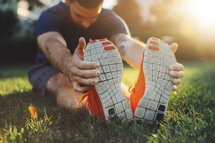 Attractive young man stretching in the park before running at the sunset focus on shoes