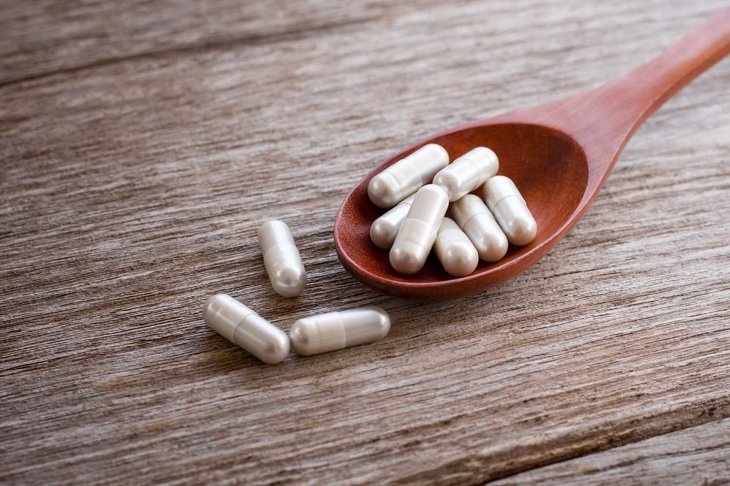 White gingsen herbal medicine capsules pill in wooden spoon isolated on wood table background.